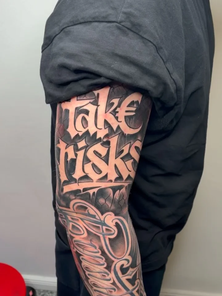 Lettering ‚Take Risks‘ auf dem Oberarm